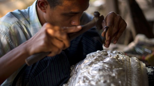 Homem esculpe imagens em uma bacia de prata em loja da região de Sagaing ao norte de Mianmar