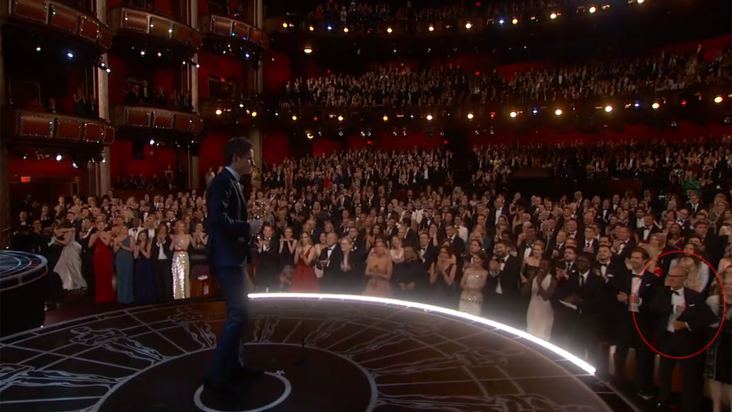 Michael Keaton (no canto inferior direito) guarda papel no paletó, enquanto Eddie Redmayne aceita o Oscar de melhor ator