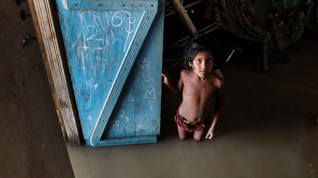 Garoto dentro de sua casa alagada durante a época de monções em Boramari, Índia