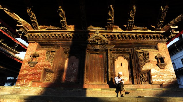 Homem senta em frente a monumento, no Nepal