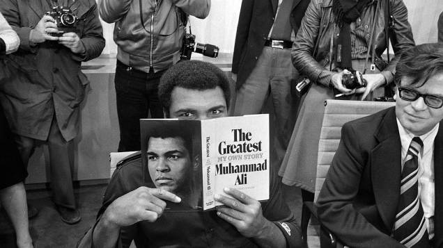 Muhammad Ali com uma cópia de sua autobiografia no aeroporto de Frankfurt, em outubro de 1975. Ele foi à cidade alemã para lançar o livro na maior feira literária do mundo