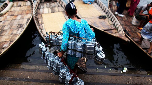 Mulher carrega cestas de alimentos em um barco, no rio Buriganga em Dhaka