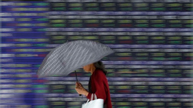 Mulher passa por painel de cotações em frente a Bolsa de Valores de Tóquio, Japão