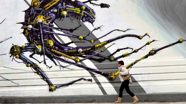 Mulher passa por muro com grafite em Atenas, Grécia