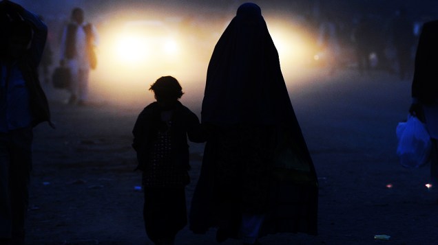 Mulher afegã acompanha uma criança ao longo de uma estrada em Cabul