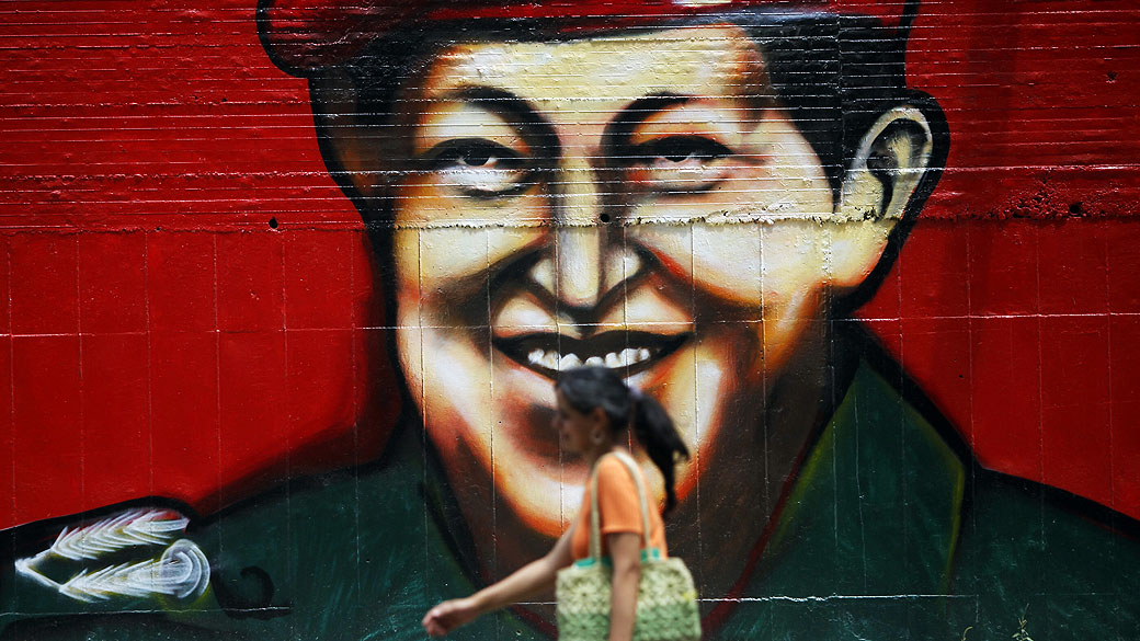 Mulher caminha em frente a muro com a figura do presidente venezuelano Hugo Chávez em Caracas