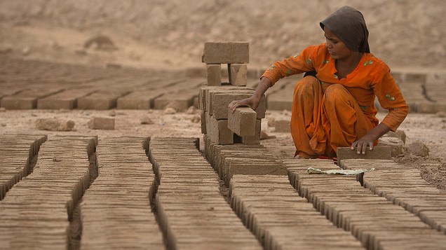 Menina arruma tijolos para ser cozidos em um forno de fábrica ao ar livre nos arredores de Islamabad