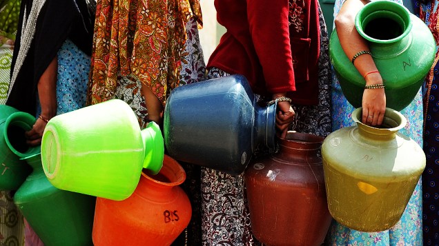 Mulheres de uma vila indiana fazem fila para abastecer seus potes com a água de um poço em Bangalore
