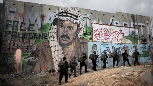 Soldados israelenses passam por muro com graffiti representando o falecido líder palestino Yasser Arafat, durante confrontos com manifestantes nas celebrações do Nakba, em Israel - 15/05/2011