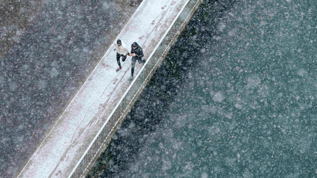 Dois corredores percorrem uma ponte sobre o rio Aare na cidade de Berna sob intensa nevasca, na Suíça