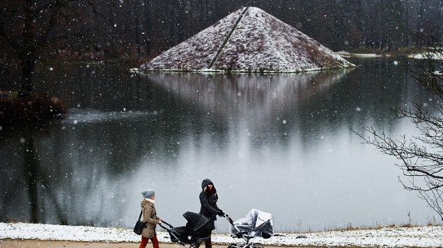 Mulheres empurram carrinho de bebê ao redor do lago no parque Fuerst-Pueckler, coberto por neve em Cottbus na Alemanha