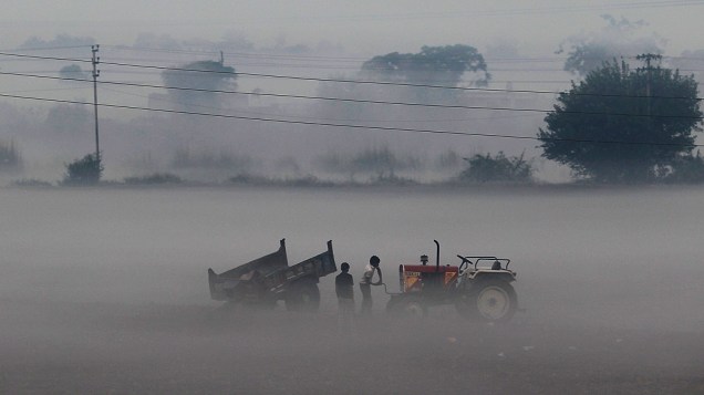 Agricultores são vistos em meio à neblina num campo ao longo da rodovia Nova Déli-Noida, na Índia