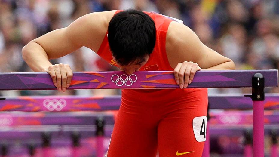 O atleta chinês Liu Xiang beija a barreira após desistir da eliminatória dos 110m com barreiras por conta de uma contusão