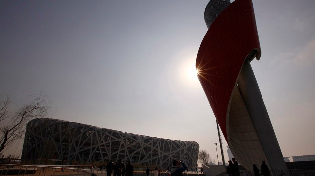 Turistas fotografam a pira olímpica, erguida do lado de for a do Ninho do Pássaro