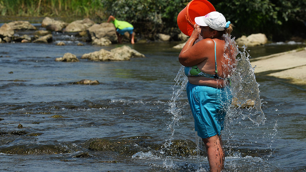 Mulher derrama um balde de água para se refrescar do calor que chegou aos 40º Celsius, no rio Arges próximo a Bucareste, na Romênia