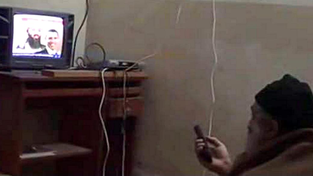 Osama bin Laden assiste a imagens de uma TV árabe em seu esconderijo, no Paquistão; na tela, ele aparece numa montagem ao lado do rosto de Barack Obama, presidente americano