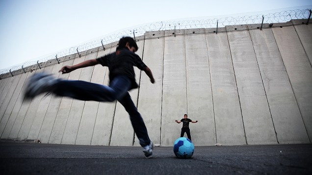 Crianças palestinas jogam bola em frente ao muro construído por Israel ao redor dos territórios palestinos, na vila de Abu Dis, Cisjordânia