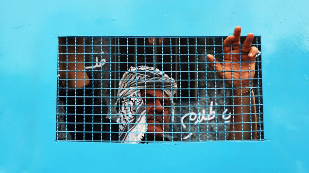 Homem palestino está acorrentado a uma gaiola durante uma manifestação na cidade de Ramallah, na Cisjordânia