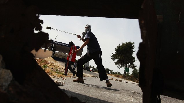 Jovem palestino usa estilingue para atirar pedra durante confronto com soldados israelenses, nas proximidades de Ramallah, na Cisjordânia