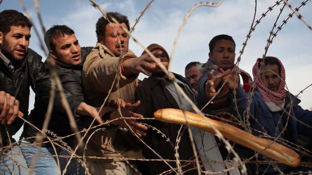 Trabalhadores famintos tentar pegar pão na cerca de arame farpado na fronteira da Tunísia