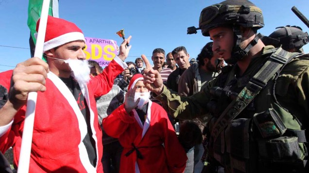 Soldado israelita enfrenta um palestino vestido de Papai Noel durante protesto contra o muro de separação israelita em Al Masara, Cisjordânia