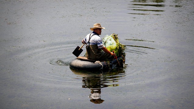 Pescador recolhe sua rede remando um barquinho improvisado em um canal de Pequim, na China<br>  