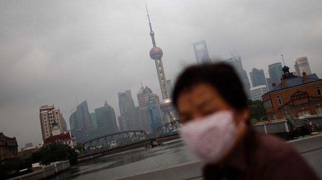 Mulher de máscara caminha ao longo do rio Huangpu. Xangai é uma das cidades mais poluídas do mundo por causa do gás carbônico e do sulfeto