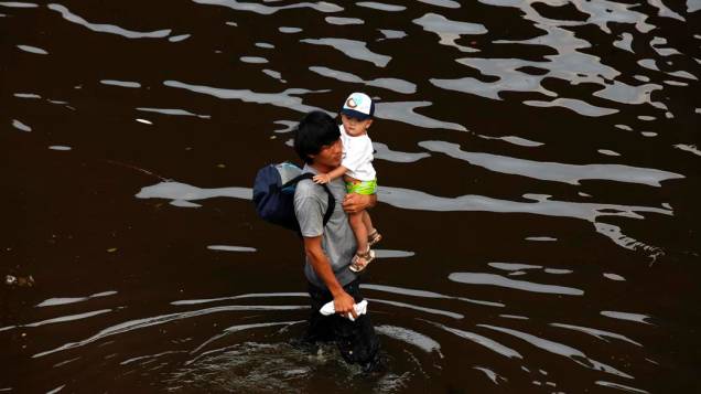 Tailandês com o filho no colo durante inundação em Bangcoc, Tailândia