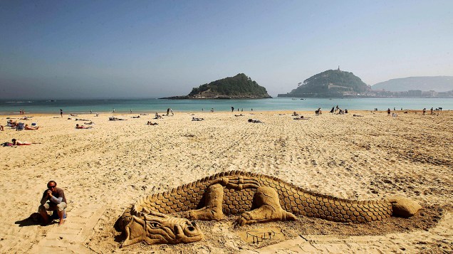 Artista anônimo descansa ao lado da escultura de um dragão feita nas areias da praia de Ondarreta, em San Sebastian, na Espanha