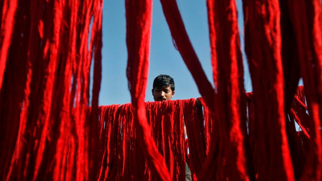 Trabalhador pendura fios tingidos para secar em fábrica têxtil na periferia de Agartala, na Índia