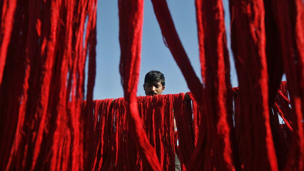 Trabalhador pendura fios tingidos para secar em fábrica têxtil na periferia de Agartala, na Índia