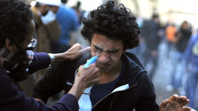 Manifestante com spray de água ajuda companheiro atingido por gás lacrimogênio durante o terceiro dia de confrontos na praça Tahrir no Cairo, Egito