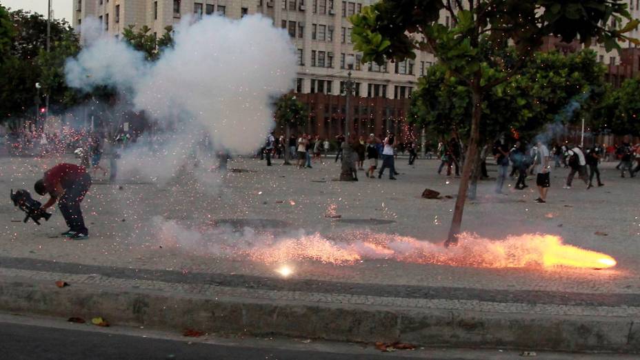 Repórter cinematográfico da TV Bandeirantes larga a câmera e cai no chão por causa do impacto do explosivo