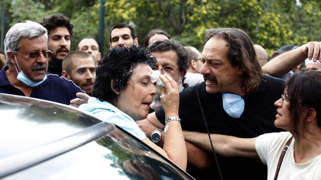 Liana Kanelli, parlamentar do partido Comunista, limpa o rosto, após ser atingida por iogurte durante protesto em frente ao Parlamento grego em Atenas