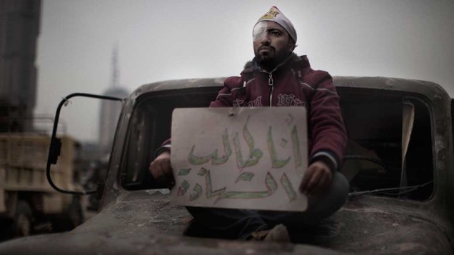 Manifestante ferido mostra cartaz "Quero ser mártir", escrito em árabe, em uma barricada do exército