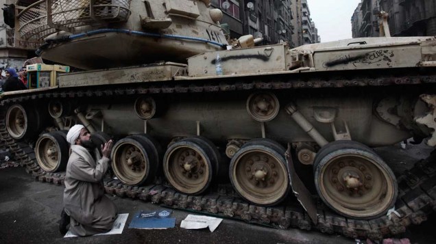 Manifestante reza ao lado de um tanque do exército egípcio durante o 12º dia de protestos no Cairo, Egito