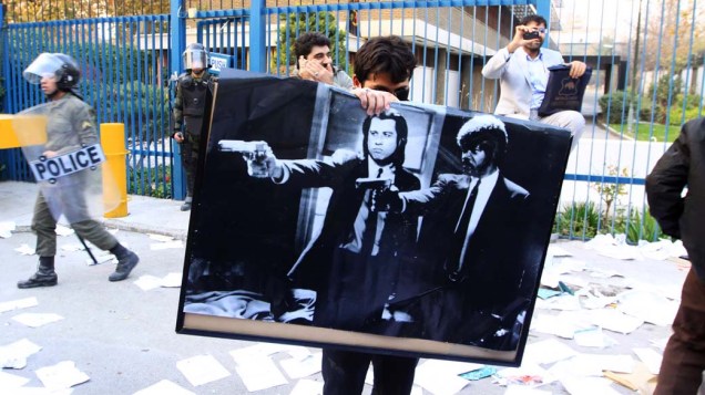 Manifestante com cartaz dos atores americanos John Travolta e Samuel L. Jackson em cena do filme "Pulp Fiction", durante protesto na embaixada britânica em Teerã, Irã