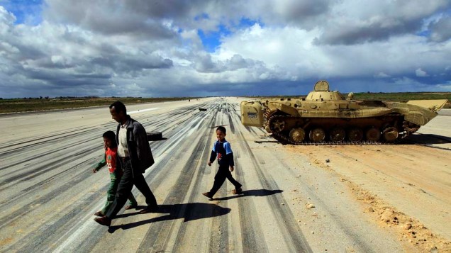 Homem caminha com criança em aeroporto militar na cidade de Al Abrak, Líbia