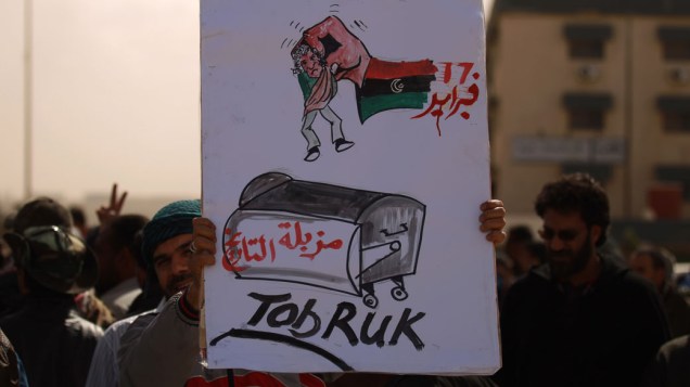 Manifestante mostra cartaz com caricatura do líder Muamar Kadafi sendo jogado em contêiner de lixo, na cidade de Trobuk, Líbia