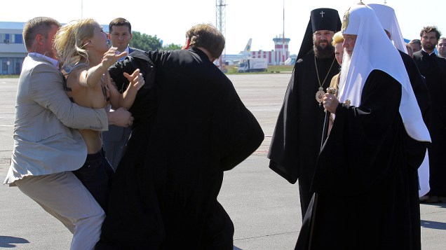 Seguranças detêm ativista do grupo feminista Femen durante protesto contra a visita do chefe da Igreja Russa Ortodoxa, o Patriarca Kirill (à direita), à Ucrânia, no aeroporto Borispol, perto da capital, Kiev