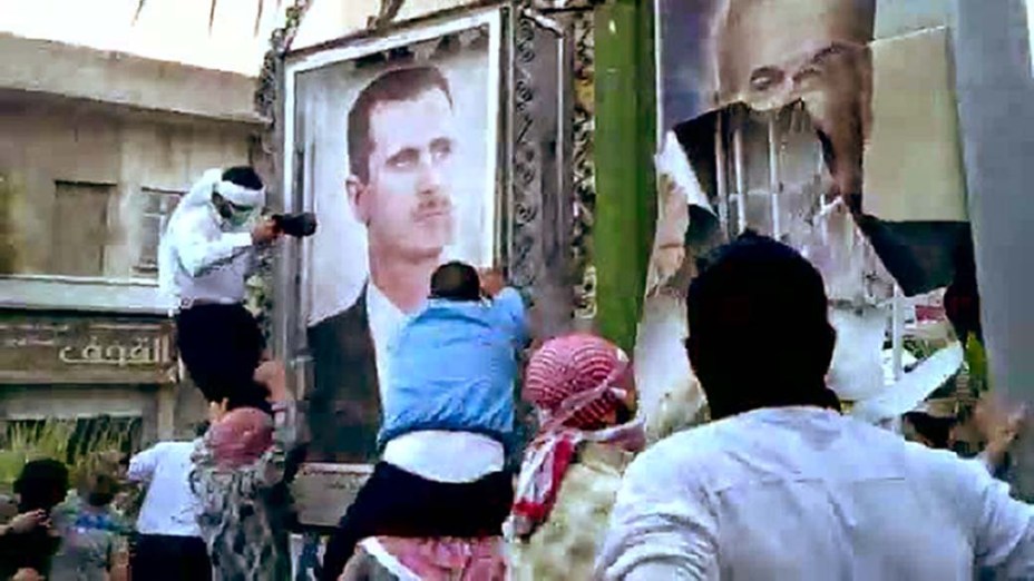 Em Hama, manifestantes anti-governo destroem retratos do ex-presidente sírio Hafez al-Assad e seu filho, o atual presidente Bashar al-Assad