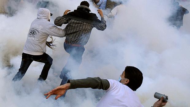 Manifestante lança bomba de gás lacrimogêneo contra a polícia enquanto outros fogem na praça Tahrir