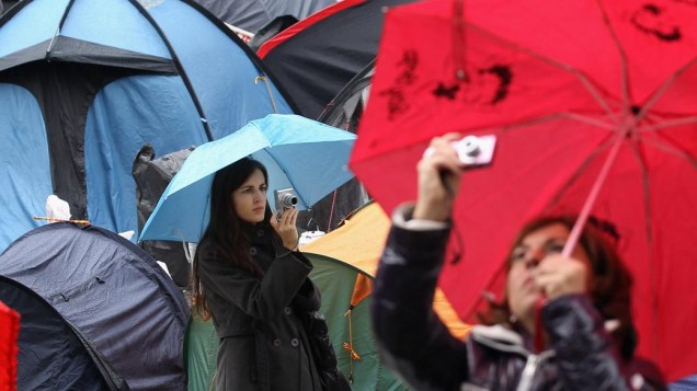 Turistas fotografam a Catedral de São Paulo enquanto manifestantes do movimento “Occupy London Stock Exchange” protestam em Londres