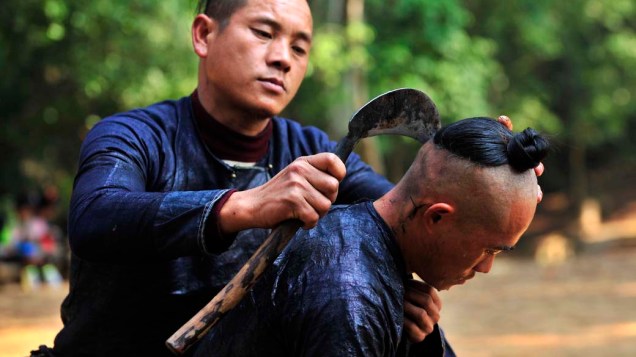 Um homem da minoria étnica Miao raspa a cabeça de outro morador com uma foice na aldeia de Basha, na China