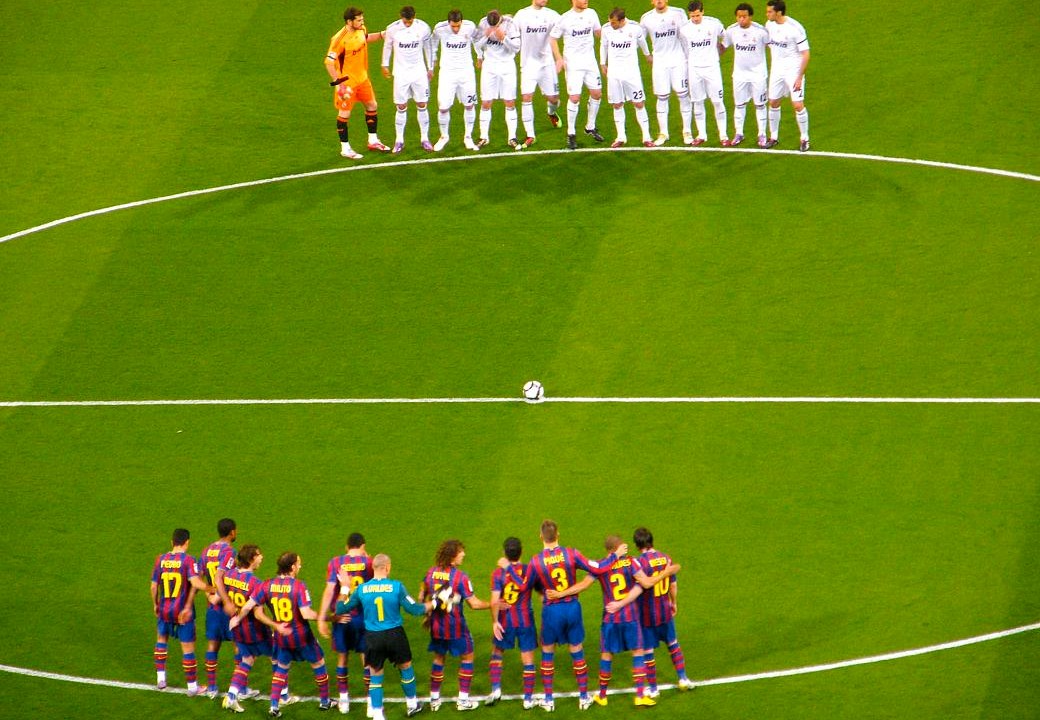 Os times do Real Madrid e do Barcelona se reúnem no centro do gramado para respeitar um minuto de silêncio antes do início da partida