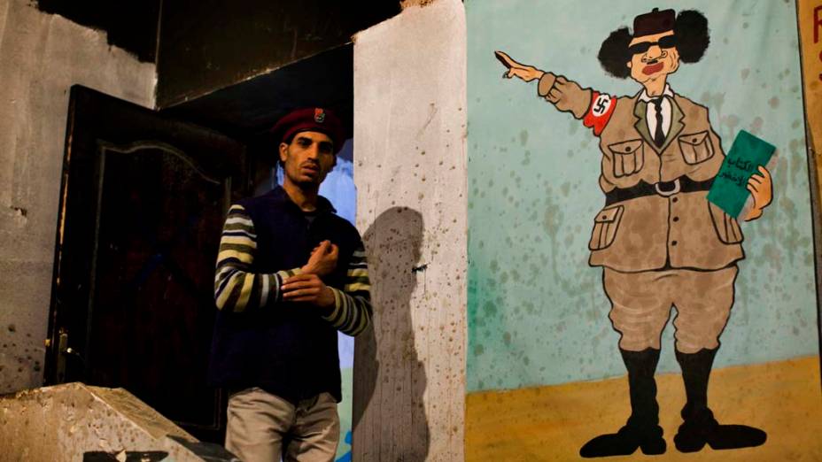 Rebelde ao lado de caricatura do ditador Muamar Kadafi, em Benghazi, Líbia