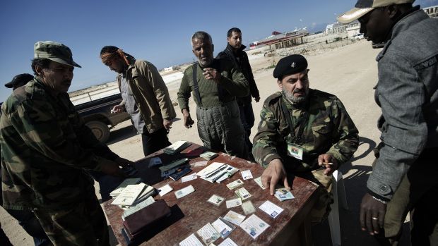 Oficiais checam documentos de pessoas tentando deixar a Líbia. Cerca de 100 mil fugiram da violência na Líbia na semana passada, em uma crescente crise humanitária, informou a agência de refugiados da ONU neste domingo