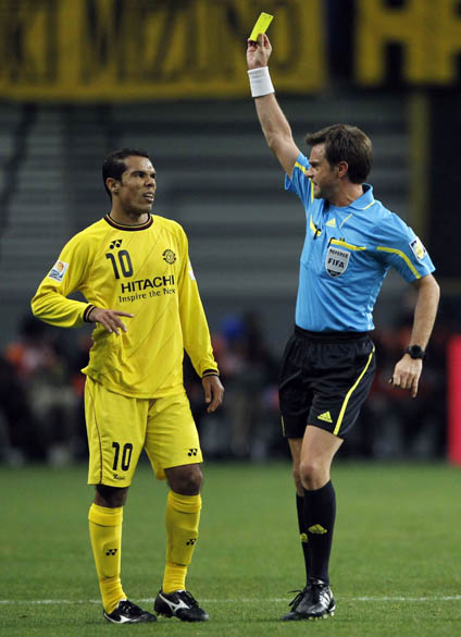 Juiz Nicola Rizzoli mostra cartão amarelo para Leandro Domingues do Kashiwa Reysol durante partida da semifinal do Mundial de Clubes da FIFA em Toyota, Japão