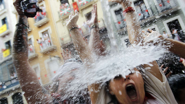 Foliões são atingidos por jato dágua lançado de uma varanda durante o festival de São Firmino, na Espanha