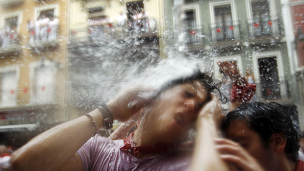 Foliões são atingidos por jato dágua lançado de uma varanda durante o festival de São Firmino, na Espanha